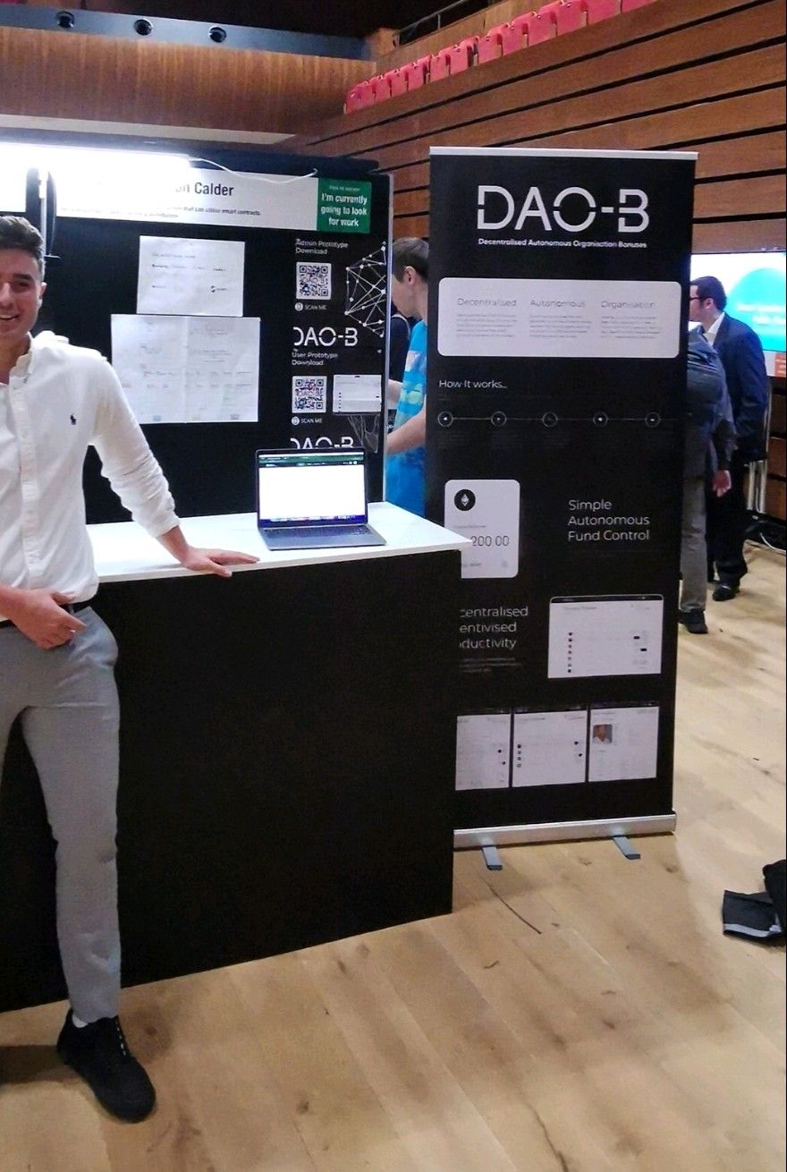 Cameron presenting the DAO-B university project beside an exhibition display